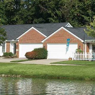 A suburban brick house with a garage and a pond in the foreground.