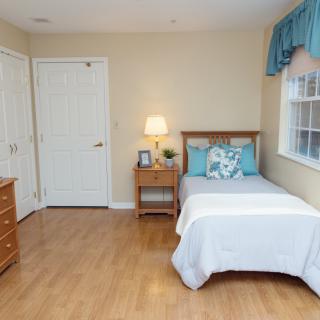 A tidy and minimalist bedroom with a single bed, nightstand, and wooden flooring.