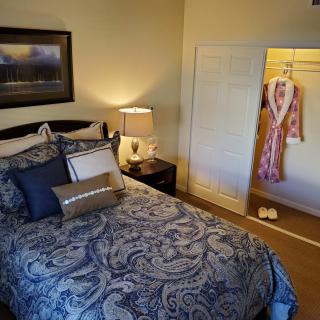 A cozy bedroom with a neatly made bed, bedside lamp, and an open closet displaying a robe.