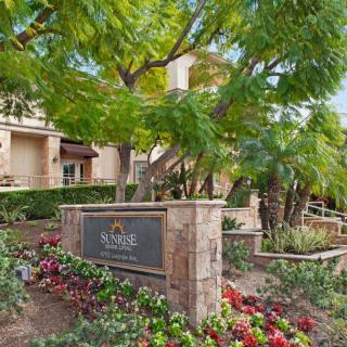 Entrance to a well-landscaped apartment complex with vibrant flowers and trees.
