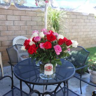 A colorful bouquet of roses placed on a glass-top outdoor table in a garden setting.