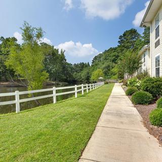 A sidewalk next to a grassy area with a white fence and trees, in a residential neighborhood.