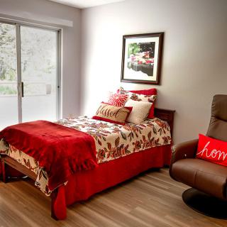 A cozy bedroom with red-themed decor featuring a single bed and a comfortable armchair.