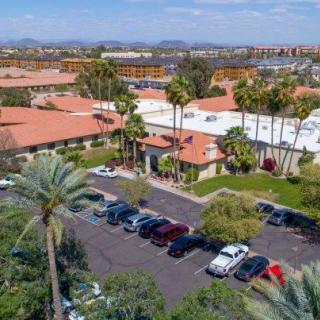 An aerial view of a property with buildings featuring red-tiled roofs, surrounded by palm trees and a parking lot filled with cars.