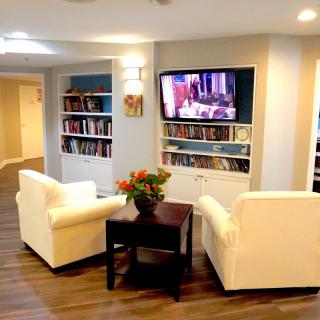 A cozy living room with two white chairs facing a television and built-in bookshelves.