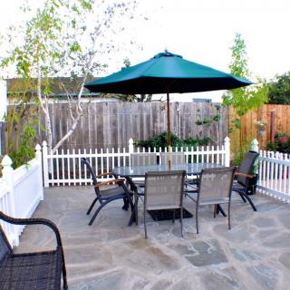 A cozy outdoor patio with a dining set and umbrella, surrounded by a white picket fence.