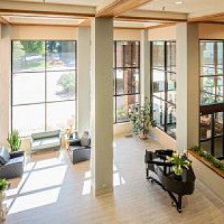 A modern lobby featuring a piano, large windows with plenty of natural light, and indoor plants.