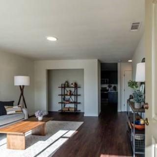 A modern living room with hardwood floors, featuring a sofa, coffee table, and shelving unit.