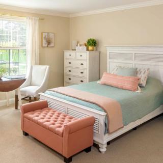 A cozy and well-decorated bedroom with a stylish bed, chest of drawers, and a soft bench at the foot of the bed.