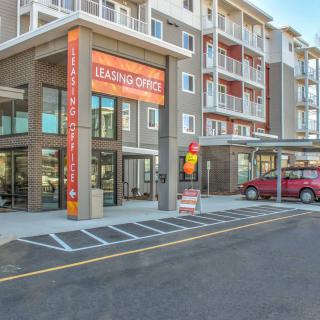 A modern apartment building with a leasing office entrance and adjacent parking lot.