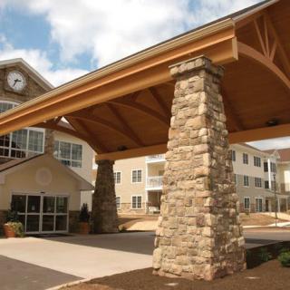 A residential building entrance with stone pillars and a clock under a clear sky.