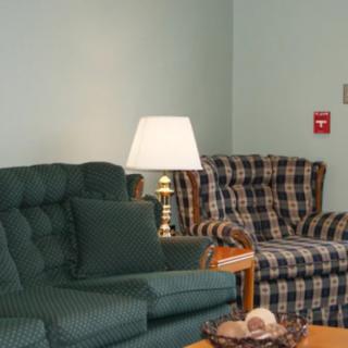 A cozy living room with a green sofa, plaid chair, and a lamp on a wooden side table.