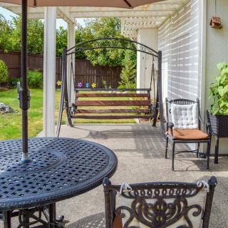 A cozy outdoor patio featuring a swing, iron table, and chairs overlooking a green backyard.