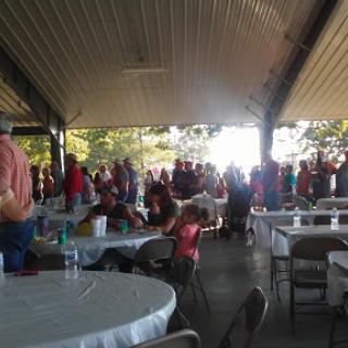 A bustling outdoor gathering with people seated at tables under a covered pavilion.