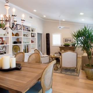 A modern dining and living area with elegant decor, featuring a chandelier, bookshelves, and an indoor plant.