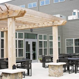 A modern outdoor patio area featuring a wooden pergola, tables, and chairs.