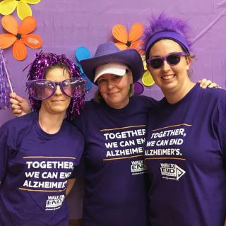 Three women wearing purple shirts and hats, participating in an Alzheimer's awareness event.