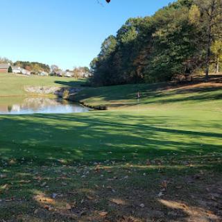 A serene view of a golf course bordered by trees and a tranquil pond.
