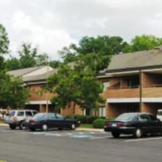 A residential area with parked cars in front of brick buildings and surrounding trees under a cloudy sky.