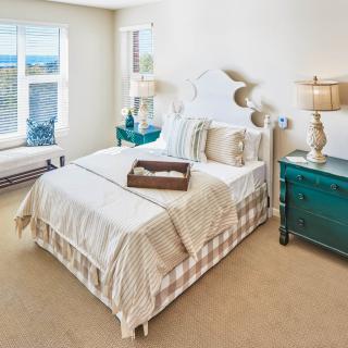A cozy bedroom interior featuring a neatly made bed, decorative pillows, and two bedside lamps under natural light from a window.