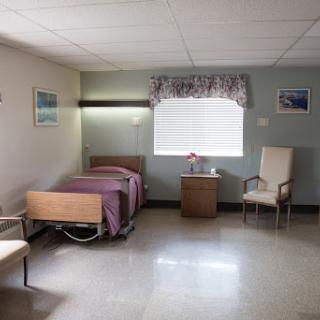 A spacious and well-lit hospital room featuring a bed, chair, and bedside table.