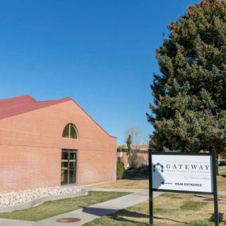 A brick building with a red roof next to a sign and tree on a clear day.