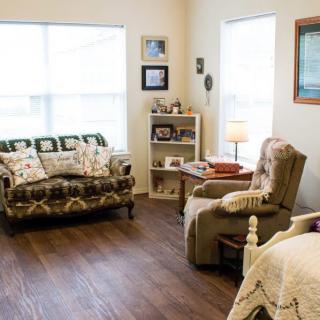 A cozy living room with a sofa, armchair, bookshelf, and table lamp.