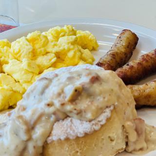 A hearty breakfast plate featuring scrambled eggs, sausage links, and biscuits smothered in gravy.