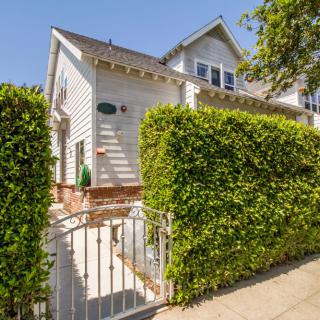 A sunny day view of a residential house with a white exterior and neatly trimmed hedges.