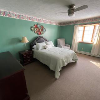 A cozy bedroom with green walls, featuring a bed, chair, window, and ceiling fan.