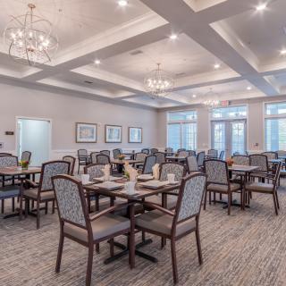 A spacious and elegantly designed dining room featuring multiple tables and chairs, with chandeliers providing ambient lighting.
