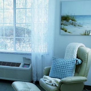 A cozy living room corner with an armchair, pillow, and blanket by a sunlit window.