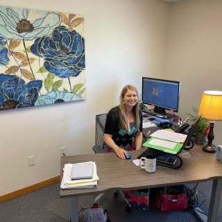A woman sits at her desk in a well-decorated office, with floral art on the wall.