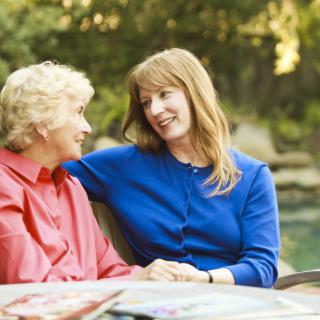 A younger woman and an elderly woman are sitting outdoors, smiling and having a conversation.