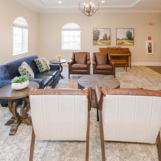 A cozy living room with a sofa, armchairs, and a coffee table, decorated with paintings and plants.