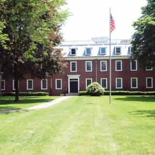 A brick building with a well-maintained lawn and an American flag on a flagpole in front.
