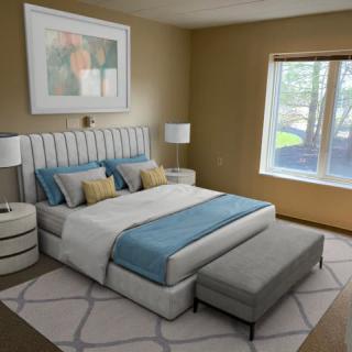A modern bedroom with a large bed, featuring blue and beige bedding, flanked by stylish nightstands and lamps. A window allows natural light to fill the room.