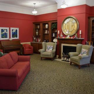 A cozy living room with red walls, featuring a sofa, armchairs, a fireplace, and bookshelves.