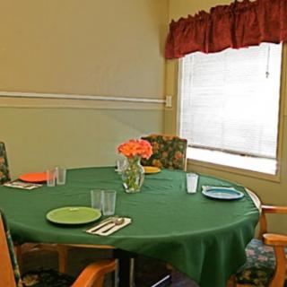 A dining table set with colorful plates, glasses, and a vase of flowers by the window.