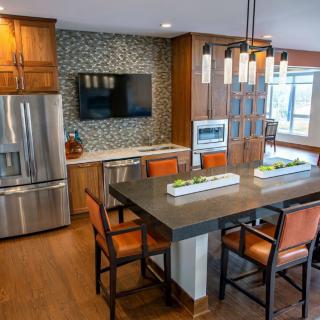 A modern kitchen with wooden cabinets, stainless steel appliances, and a stylish dining area featuring pendant lighting and bar stools.