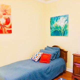 A cozy bedroom with a single bed, colorful artworks on the walls, and vibrant pillows.