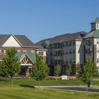 A scenic view of residential buildings surrounded by trees and a well-maintained lawn on a sunny day.