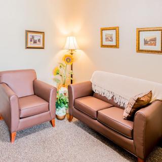 A cozy living room with a sofa, armchair, decorative lamp, and framed pictures.