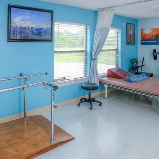 A bright physical therapy room equipped with parallel bars and a bed.