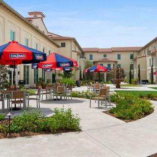 An outdoor patio area with tables, chairs, and umbrellas surrounded by landscaped buildings.