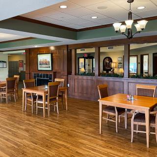 An empty dining area with wooden tables and chairs, featuring a chandelier and laminate flooring.