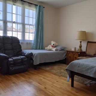 A cozy bedroom with two beds, a recliner, and natural lighting.
