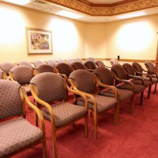 An empty conference room with rows of chairs neatly arranged on a red carpet.