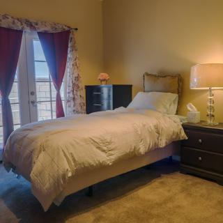 A cozy bedroom with a single bed, nightstand, and lamp next to French doors covered by curtains.
