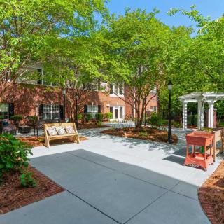 A peaceful courtyard with greenery, a bench, and a gazebo next to a brick building.